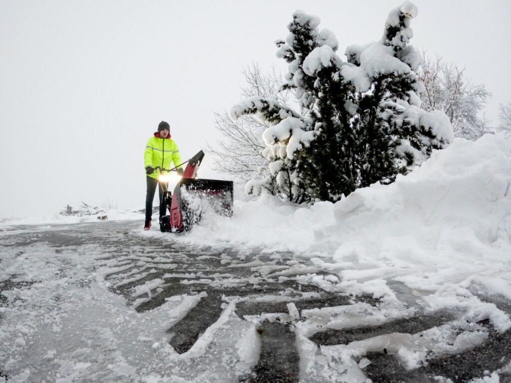Young man clearing snow of a driveway with a red snowblower